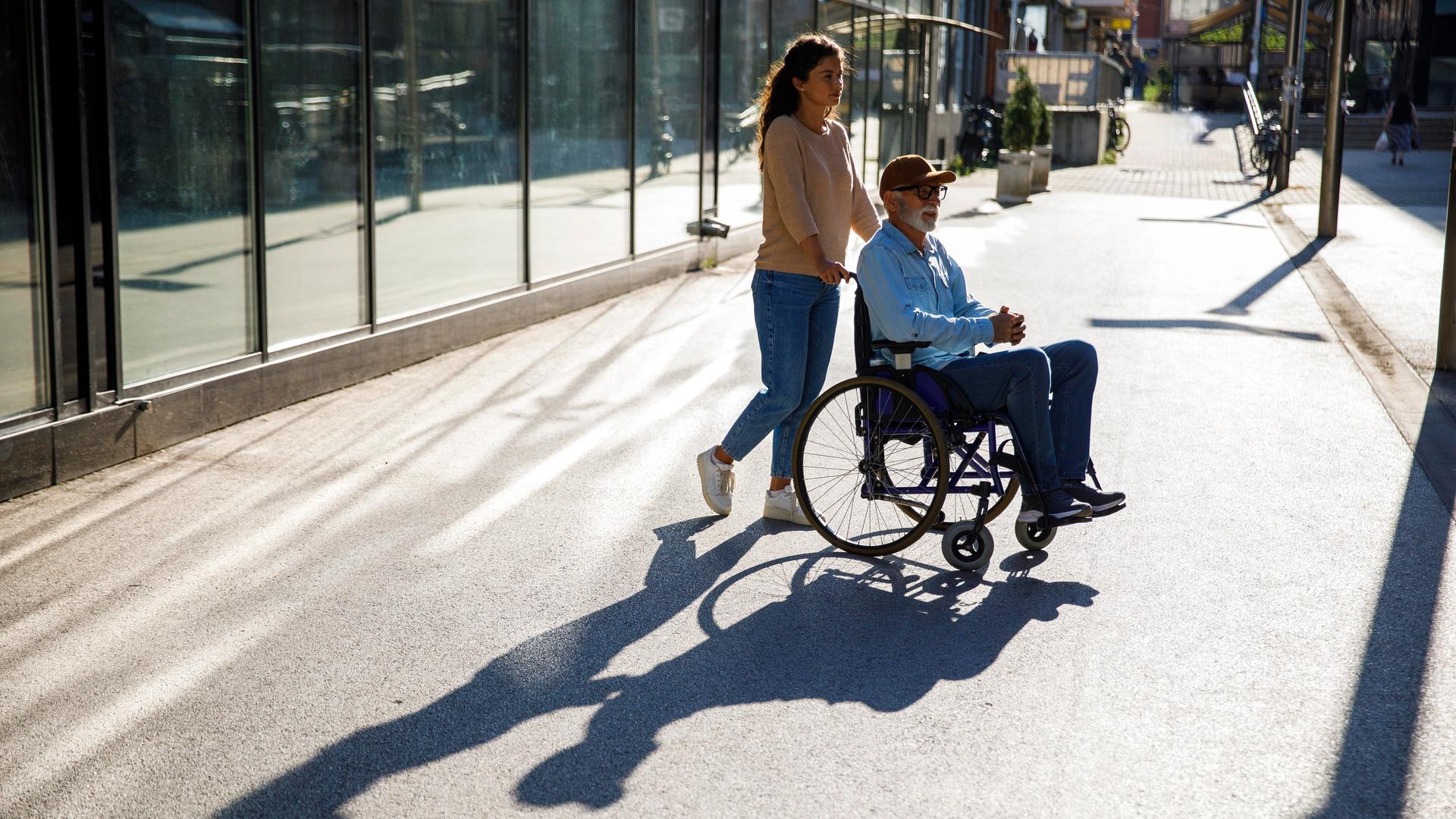 Junge Frau schiebt älteren Mann im Rollstuhl