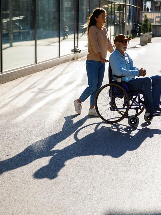 Junge Frau schiebt älteren Mann im Rollstuhl