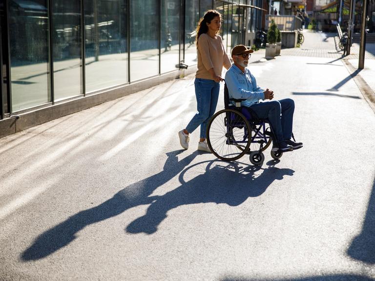 Junge Frau schiebt älteren Mann im Rollstuhl