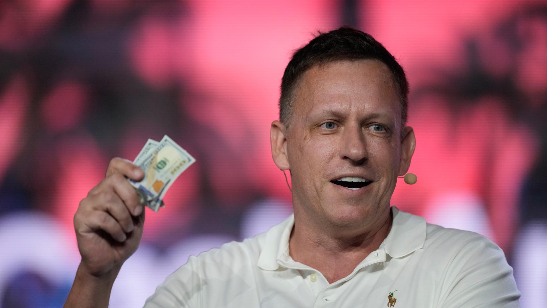 Der US-amerikanische Investor Peter Thiel hält mehrere Dollar-Scheine in der Hand.