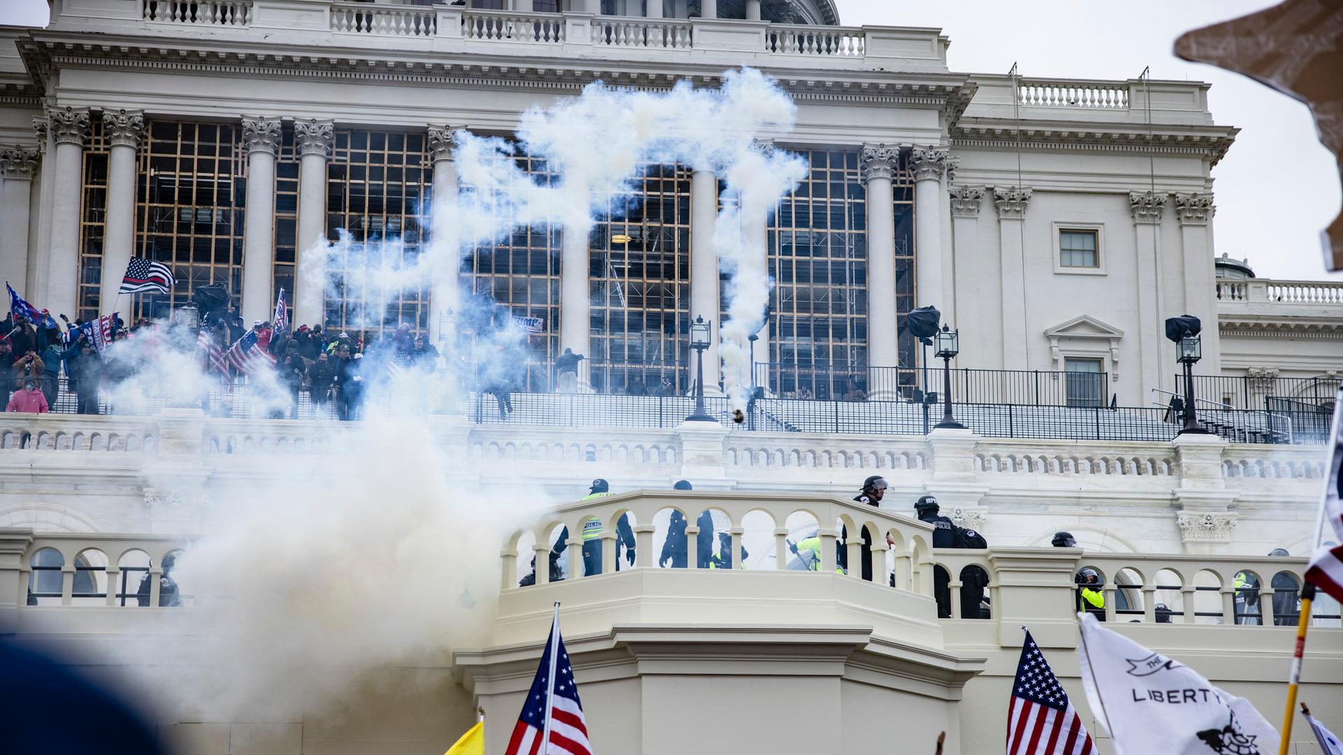 Unterstützer von Donald Trump stürmen das Kapitol in Washington DC, man sieht Flaggen und Rauch.