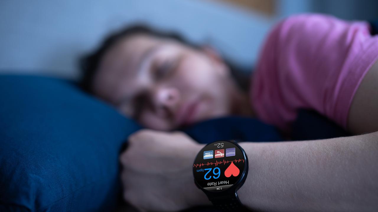 Eine Person liegt im Bett. Am Handgelenk trägt sie eine Smartwatch. Diese registriert verschiedene Körperfunktionen.  