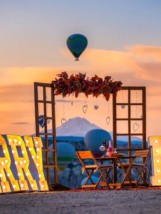 Große leuchtende Schriftzeichen "Marry me" stehen am Strand, inklusive Holrahmen und dekoriertem Tisch mit Stühlen