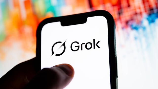 Ein Daumen tippt auf einen Smartphone-Bildschirm, auf dem "Grok" steht.