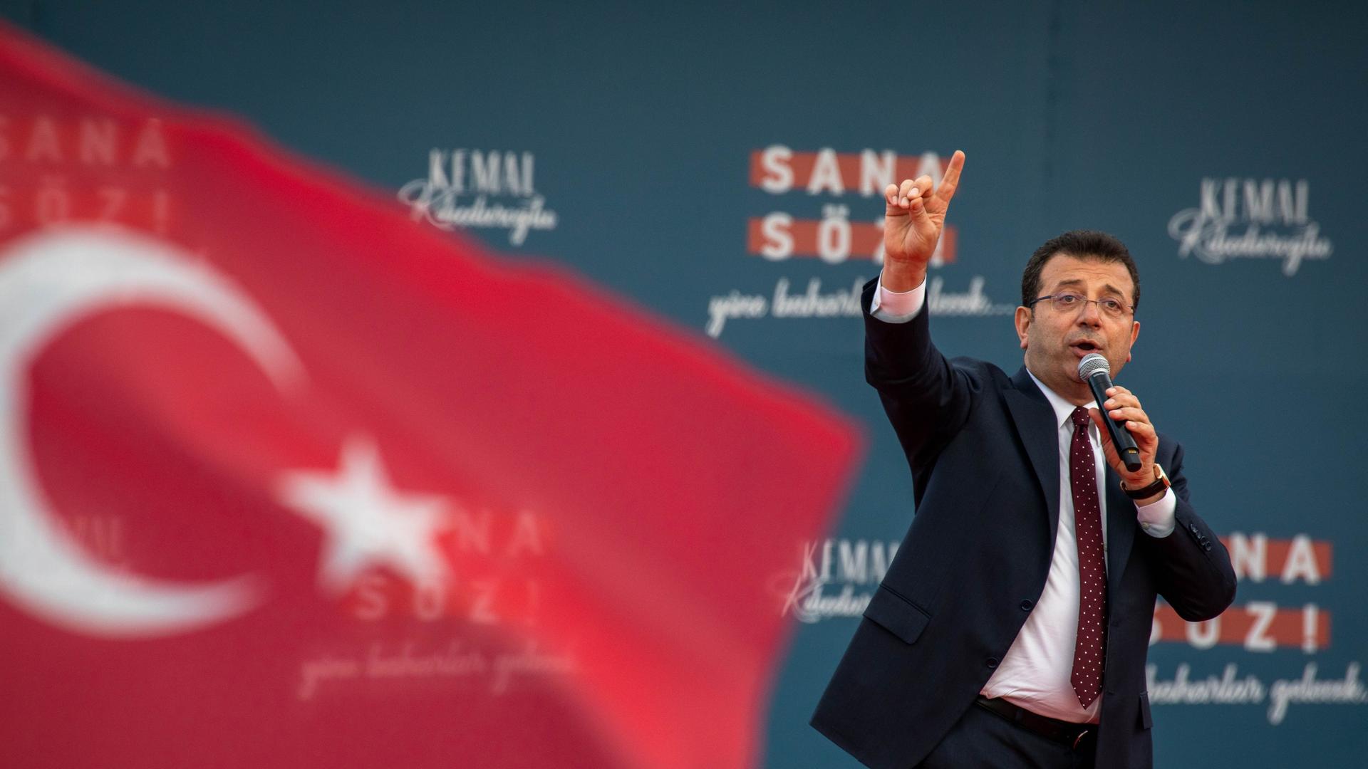 Istanbuls ehemaliger Bürgermeister Ekrem İmamoğlu spricht in ein Mikrofon, rechts von ihm die türkische Fahne.