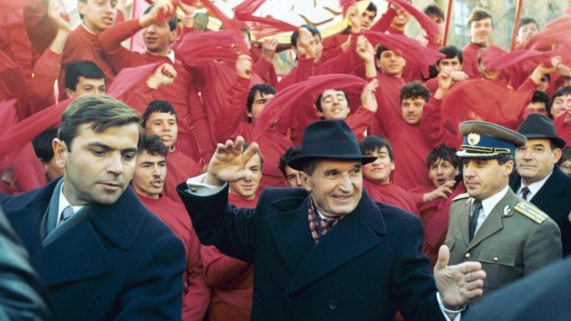 Der rumänische Diktator Nicolae Ceaușescu winkt am 24. November 1989 nach dem Parteitag in Bukarest der Bevölkerung zu. Im Hintergrund rot gekleidete junge Männer, die rote Tücher schwenken. Der rumänische Diktator Nicolae Ceaușescu winkt am 24. November 1989 nach dem Parteitag in Bukarest der Bevölkerung zu. Im Hintergrund rot gekleidete junge Männer, die rote Tücher schwenken.