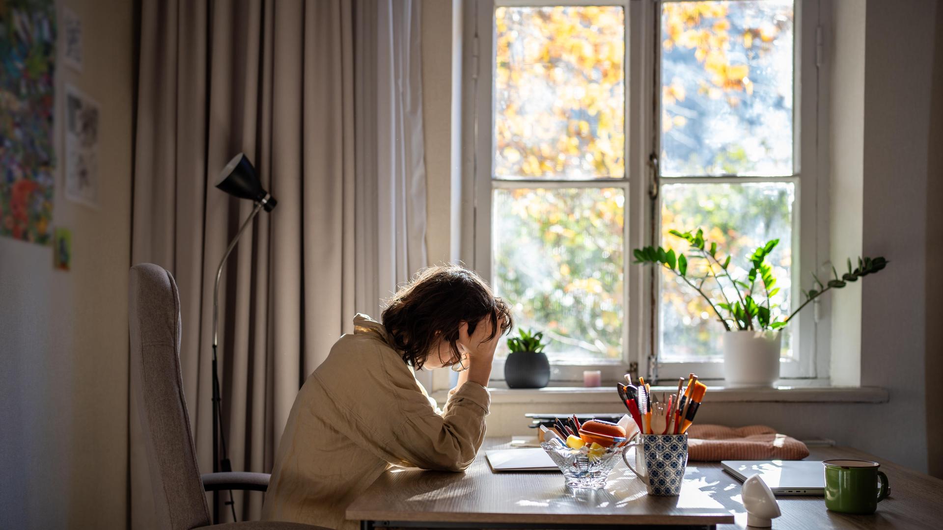 Eine offensichtlich verschlafene, halbwache Frau sitzt an einem Tisch und stützt den Kopf auf ihre rechte Hand