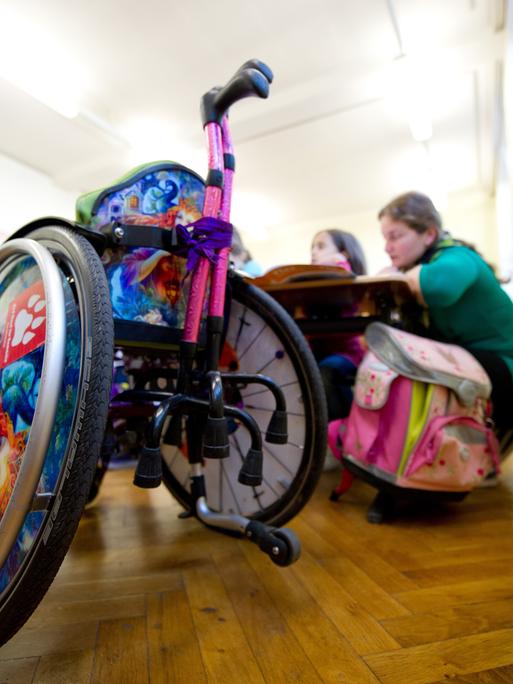 Ein Rollstuhl steht im Klassenzimmer, dahinter sitzen zwei Schülerinnen an einem Tisch