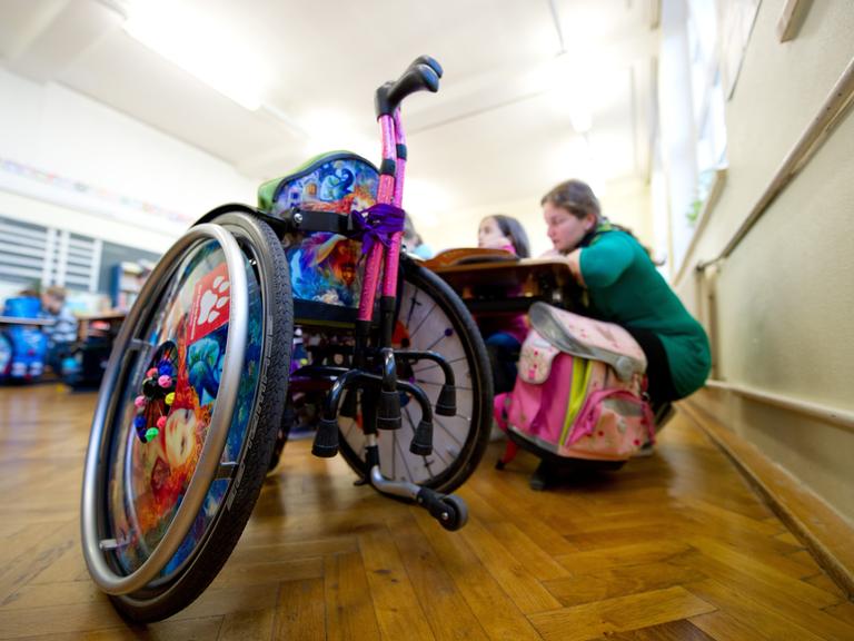 Ein Rollstuhl steht im Klassenzimmer, dahinter sitzen zwei Schülerinnen an einem Tisch