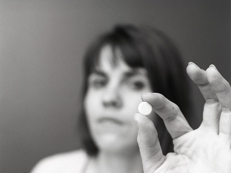 Eine Frau hält eine weiße Pille zwischen ihren Fingern. Eine Illustration für die Einnahme von Medikamenten oder für Antibabypillen zu dieser Zeit. Schweden 1971