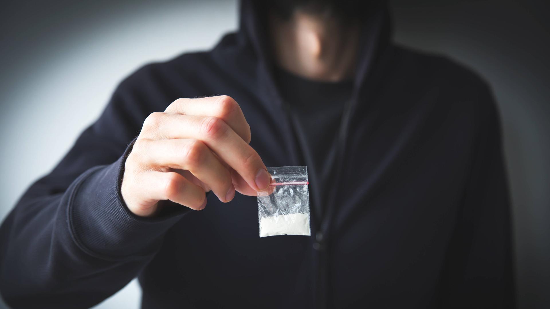 Person in Sweatshirt und Kapuzenpulli hält kleine Tüte mit weißer Substanz Person in Sweatshirt und Kapuzenpulli hält kleine Tüte mit weißer Substanz