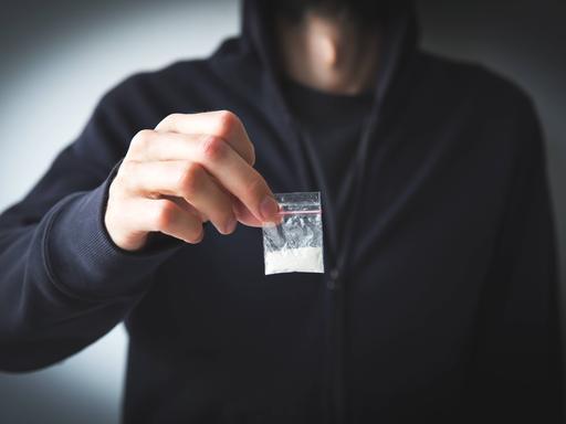 Person in Sweatshirt und Kapuzenpulli hält kleine Tüte mit weißer Substanz