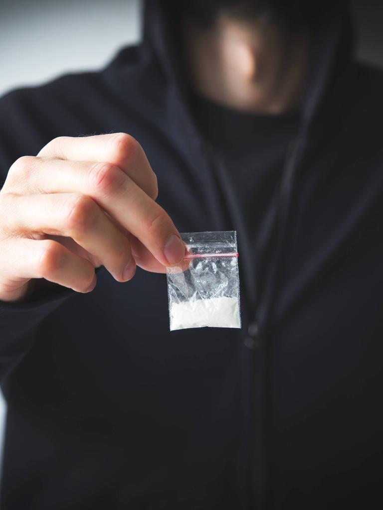 Person in Sweatshirt und Kapuzenpulli hält kleine Tüte mit weißer Substanz