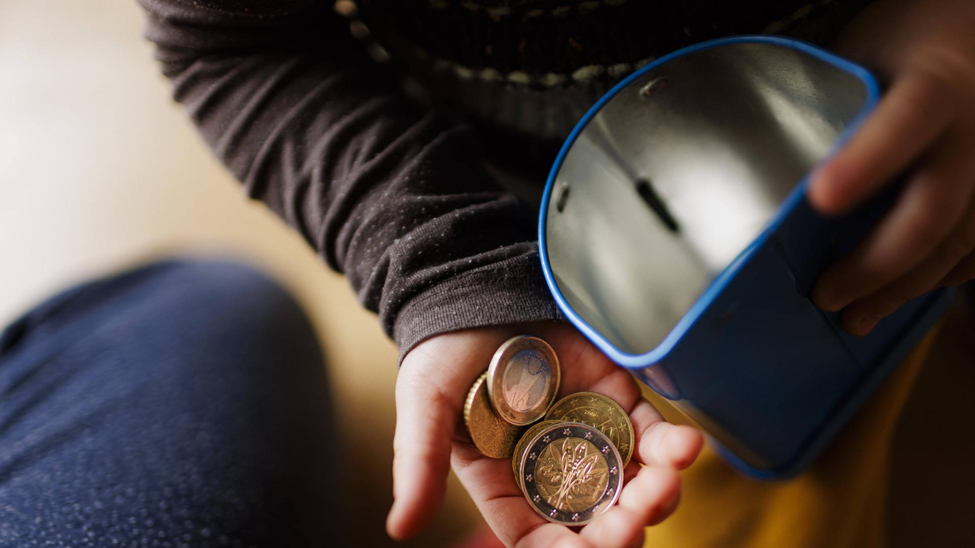 Geldmünzen in einer Kinderhand und eine Blechdose