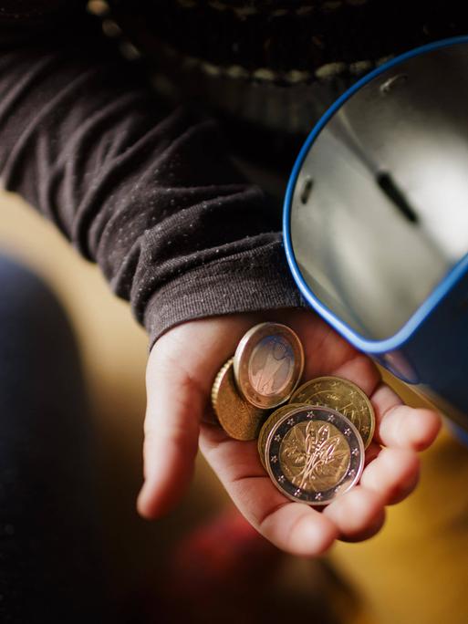 Geldmünzen in einer Kinderhand und eine Blechdose Geldmünzen in einer Kinderhand und eine Blechdose