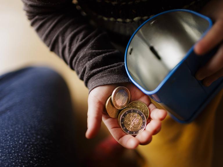 Geldmünzen in einer Kinderhand und eine Blechdose Geldmünzen in einer Kinderhand und eine Blechdose