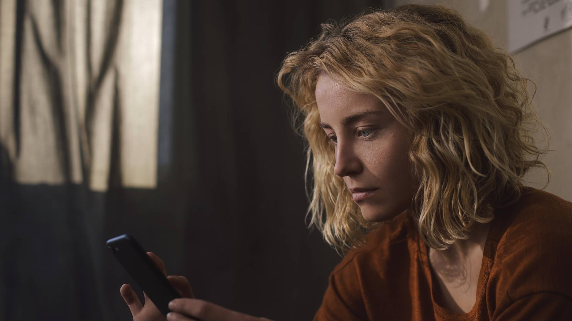 Foto einer jungen Frau, die ernst auf ihr Smartphone blickt