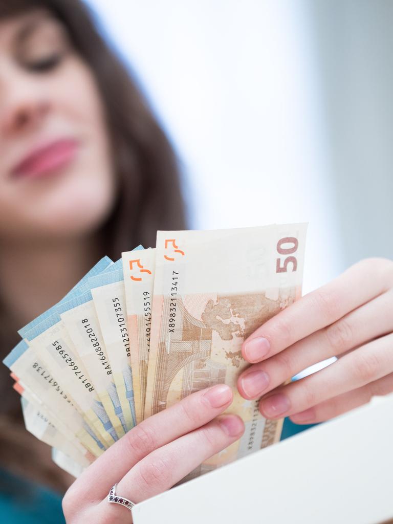 Foto der Hände einer jungen Frau, die Euro-Scheine aufgefächert in der Hand hält, das Gesicht unscharf dahinter im Hintergrund Foto der Hände einer jungen Frau, die Euro-Scheine aufgefächert in der Hand hält, das Gesicht unscharf dahinter im Hintergrund