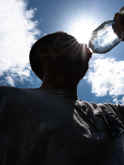 Person trinkt unter direkter Sonneneinstrahlung aus Wasserflasche Person trinkt unter direkter Sonneneinstrahlung aus Wasserflasche