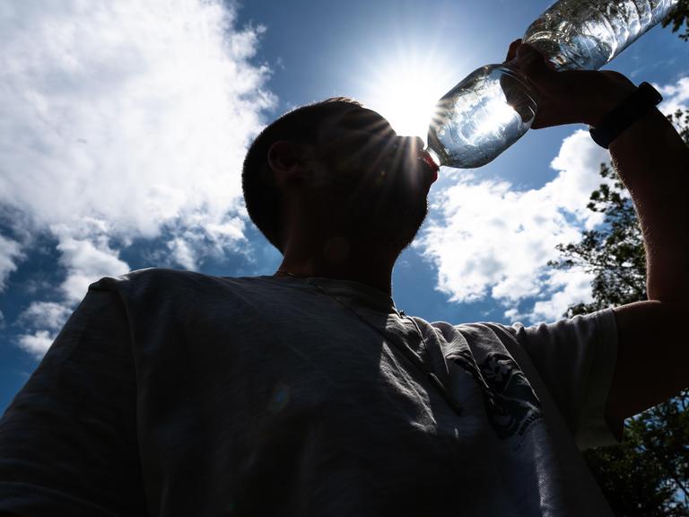 Person trinkt unter direkter Sonneneinstrahlung aus Wasserflasche Person trinkt unter direkter Sonneneinstrahlung aus Wasserflasche