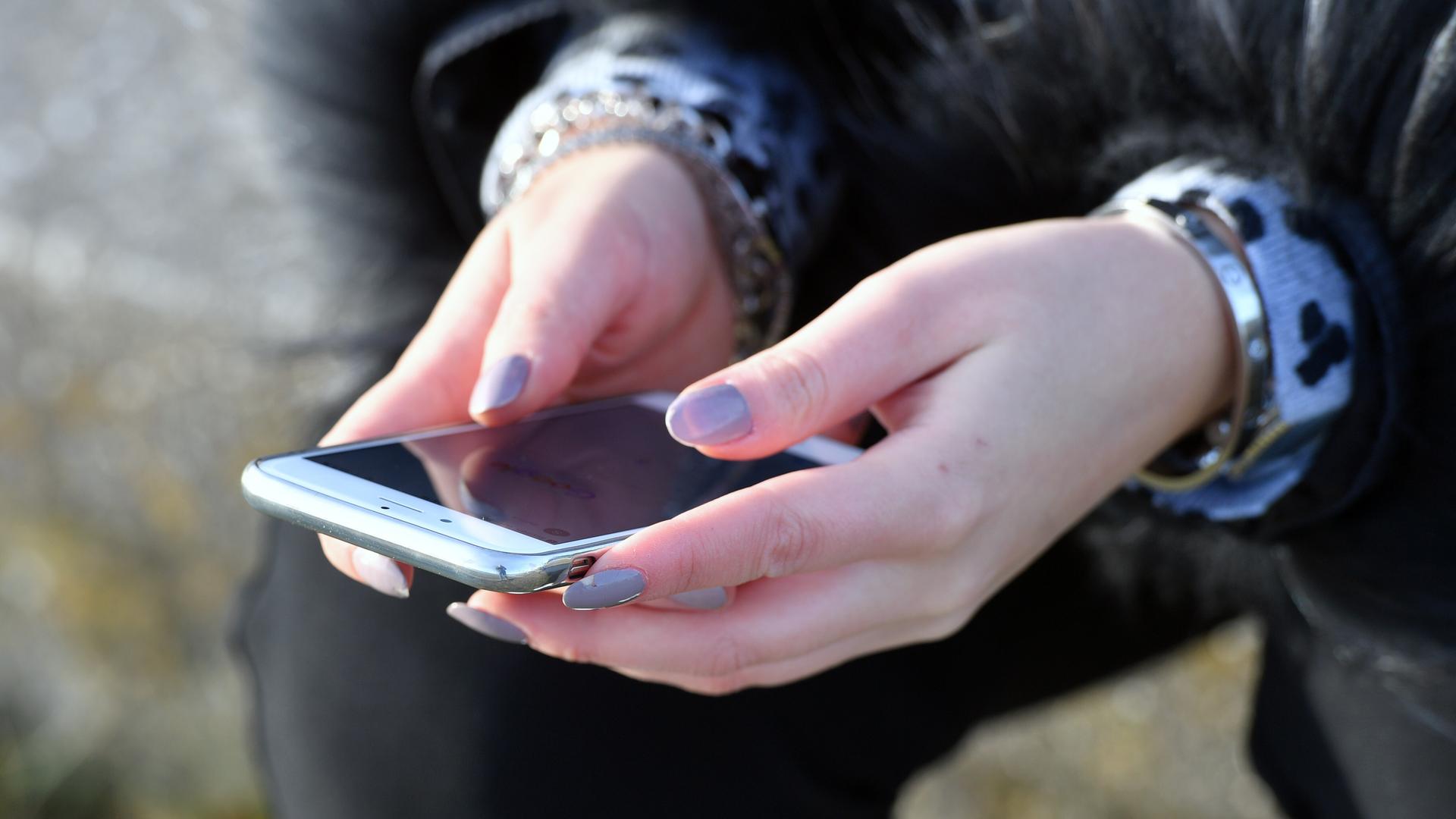 Person hält Smartphone in Händen, deren Fingernägel lang sind und lila lackiert sind