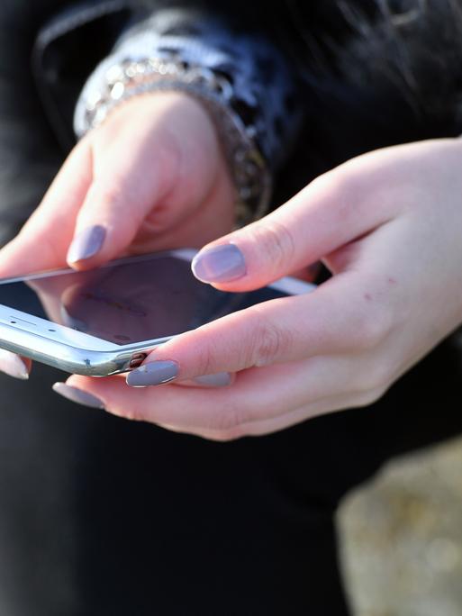 Person hält Smartphone in Händen, deren Fingernägel lang sind und lila lackiert sind