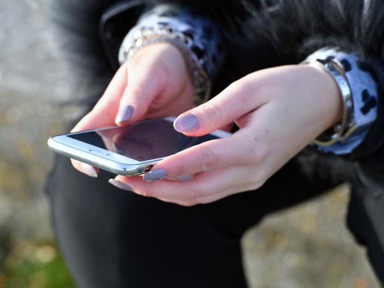 Person hält Smartphone in Händen, deren Fingernägel lang sind und lila lackiert sind