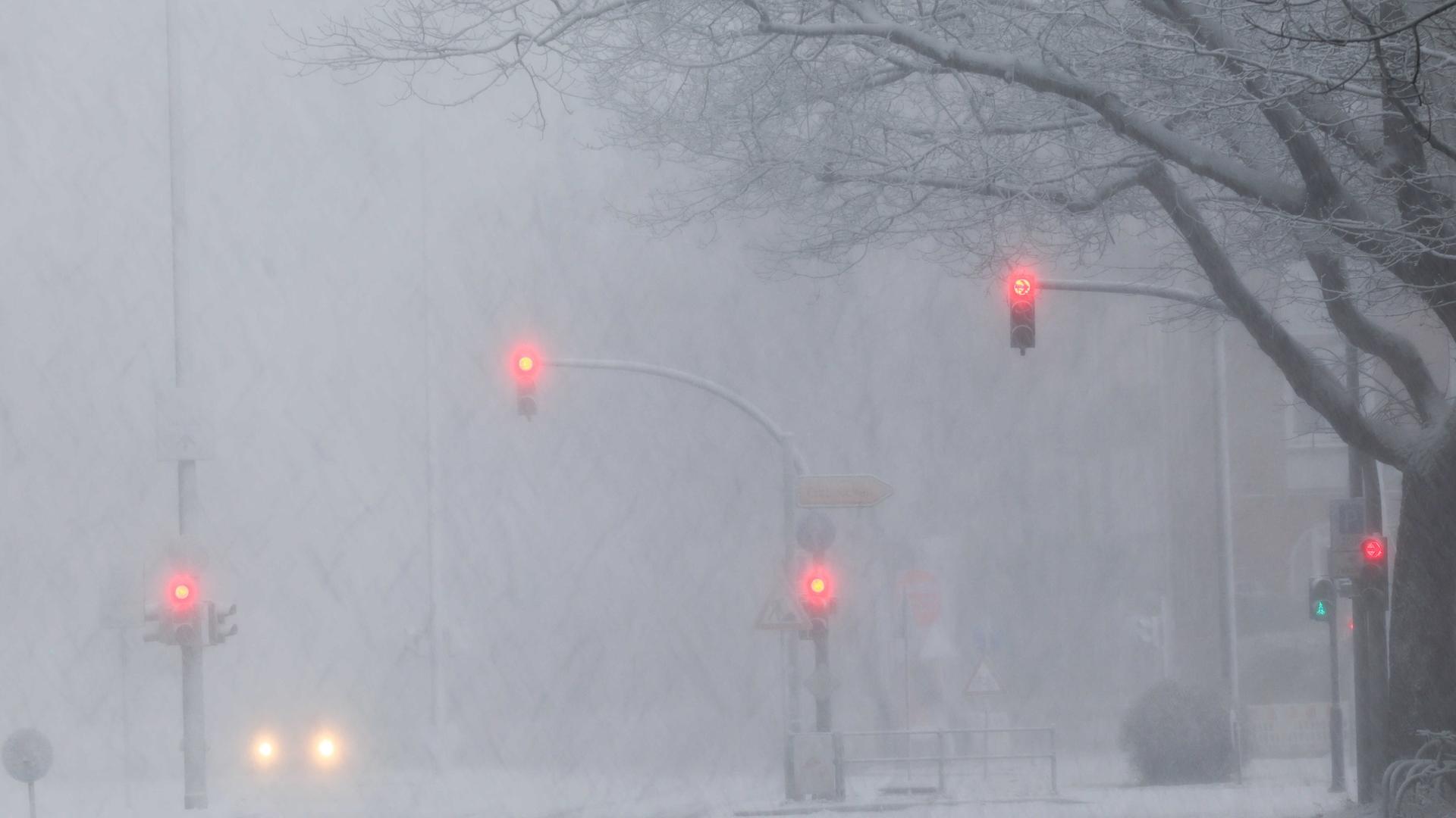 Scheinwerfer eines Autos und rot leuchtende Ampeln sind auf einer schneebedeckten Verkehrsstraße Scheinwerfer eines Autos und rot leuchtende Ampeln sind auf einer schneebedeckten Verkehrsstraße