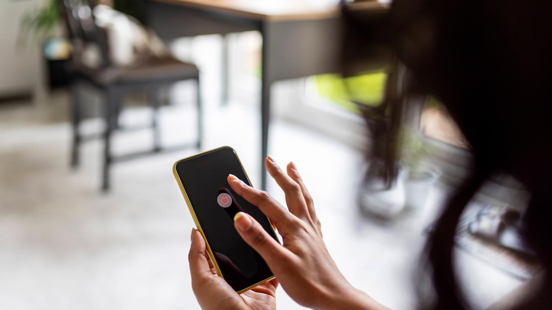 Eine Frau hält ein Handy in der Hand. Auf dem Handybildschirm wird die Möglichkeit angezeigt, das Handy auszuschalten. Eine Frau hält ein Handy in der Hand. Auf dem Handybildschirm wird die Möglichkeit angezeigt, das Handy auszuschalten.