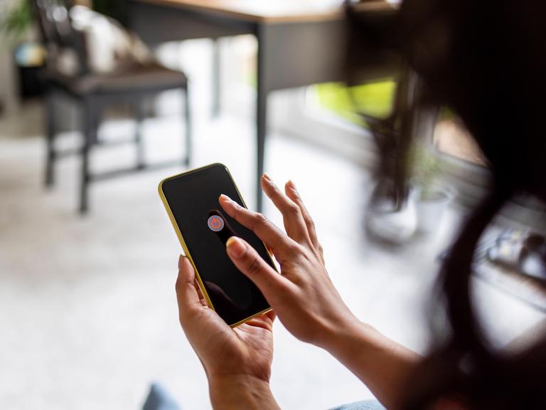 Eine Frau hält ein Handy in der Hand. Auf dem Handybildschirm wird die Möglichkeit angezeigt, das Handy auszuschalten.