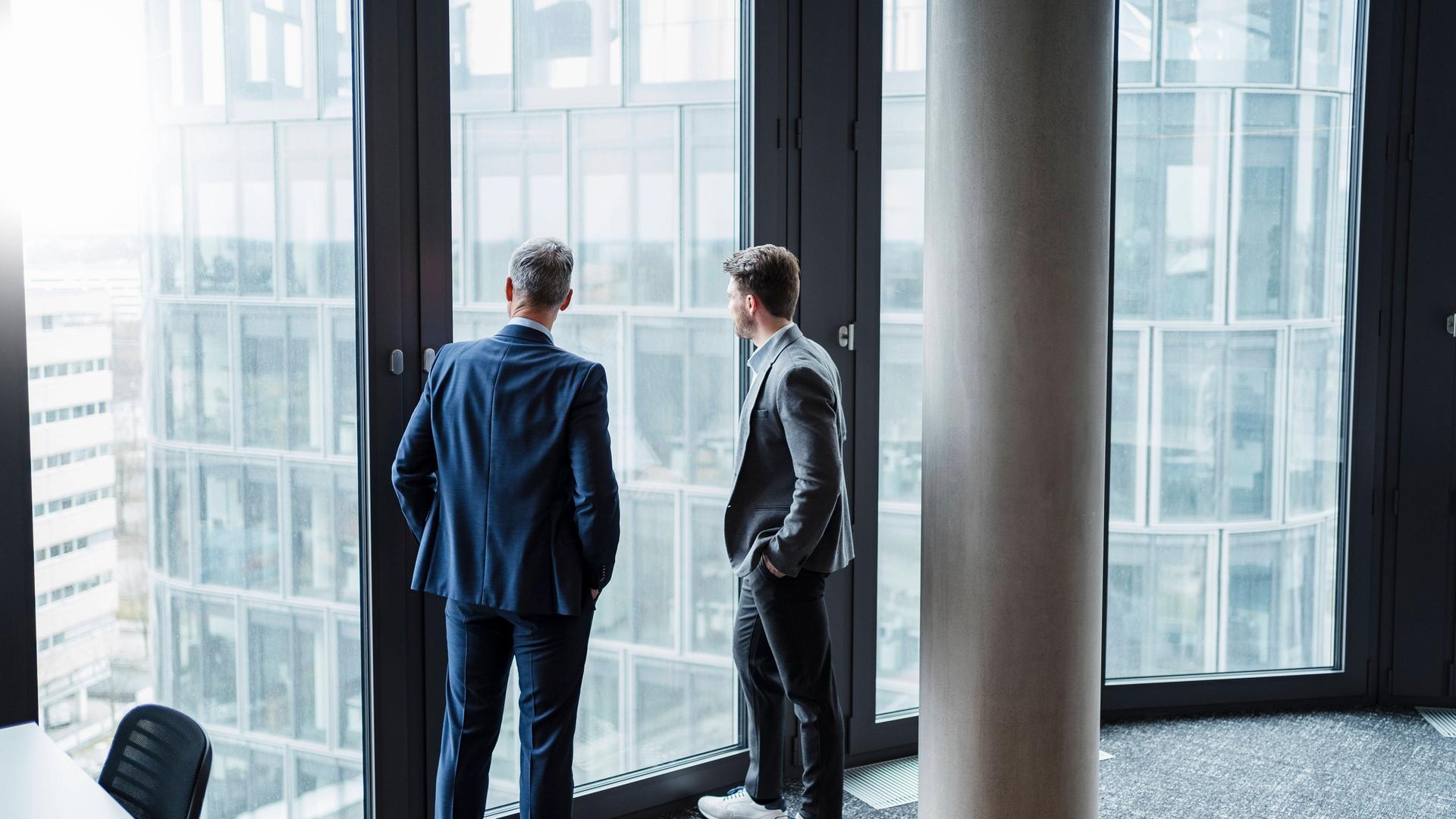 Geschäftsmann und sein Sohn/Nachfolger blicken durchs Fenster in Büro (Symbolfoto)