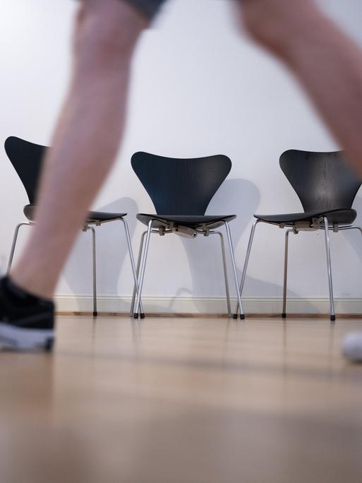 Sneaker tragende Person geht auf einem Gang an einer Reihe von Stühlen vorbei