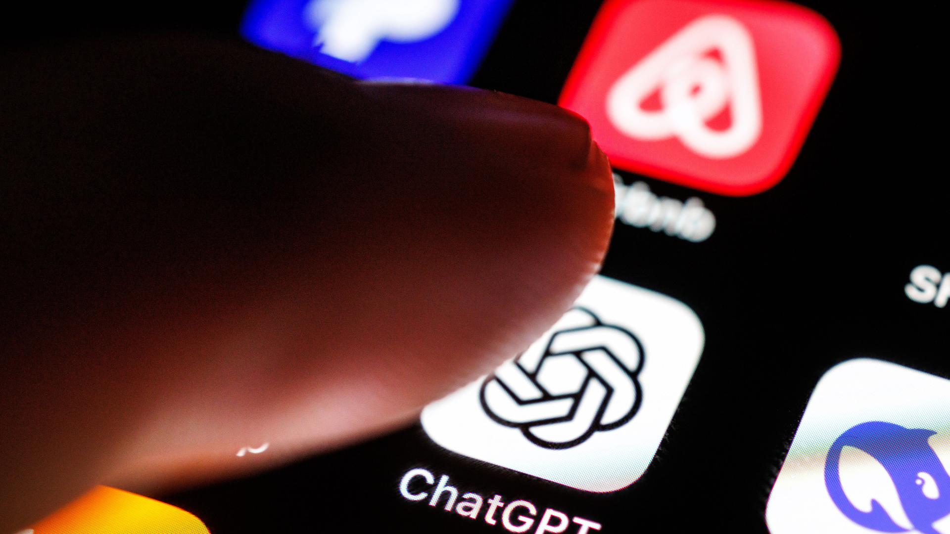 Das Logo der App ChatGPT ist auf dem Display von einem Smartphone zu sehen, während ein Zeigefinger sich dem Symbol der Applikation nähert Das Logo der App ChatGPT ist auf dem Display von einem Smartphone zu sehen, während ein Zeigefinger sich dem Symbol der Applikation nähert