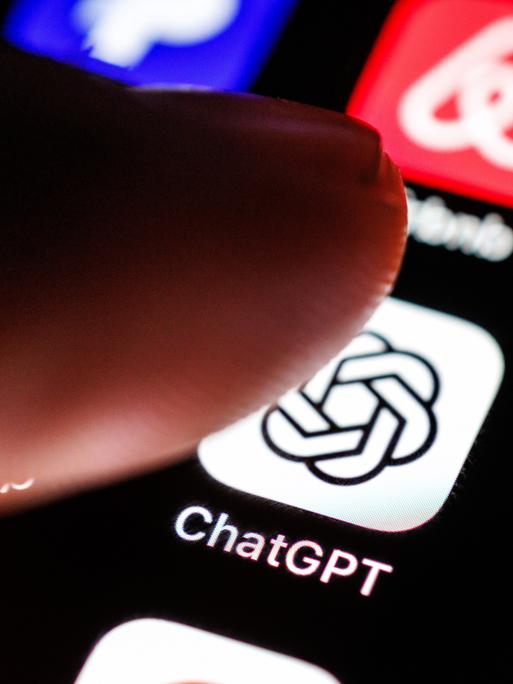 Das Logo der App ChatGPT ist auf dem Display von einem Smartphone zu sehen, während ein Zeigefinger sich dem Symbol der Applikation nähert