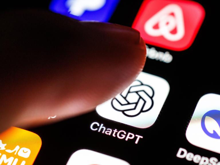 Das Logo der App ChatGPT ist auf dem Display von einem Smartphone zu sehen, während ein Zeigefinger sich dem Symbol der Applikation nähert