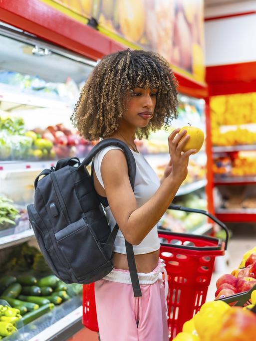 Eine Frau ist im Supermarkt einkaufen und hält einen Apfel in der Hand