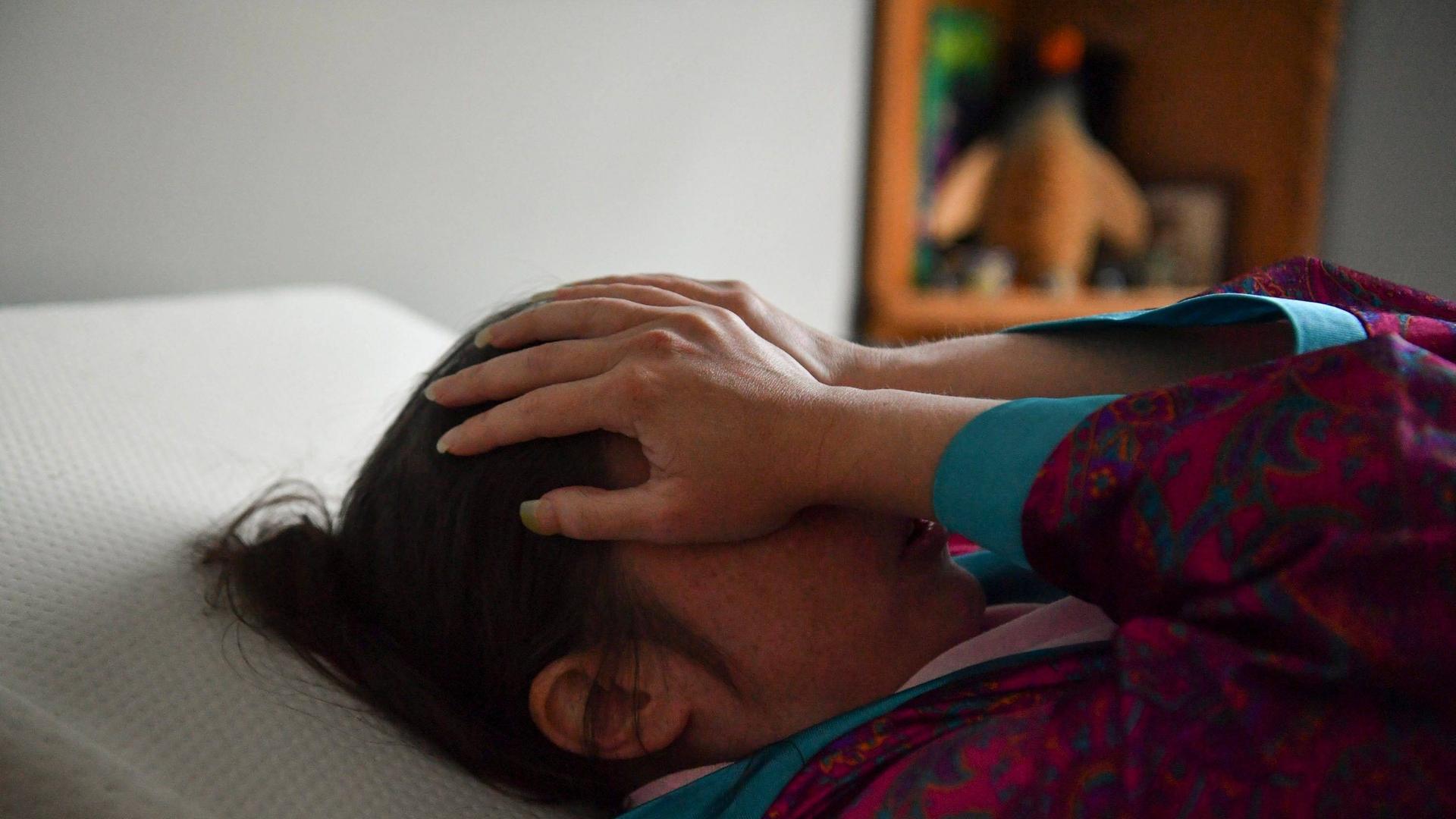 Eine Frau liegt auf einem Bett und schlägt die Hände vor ihr Gesicht