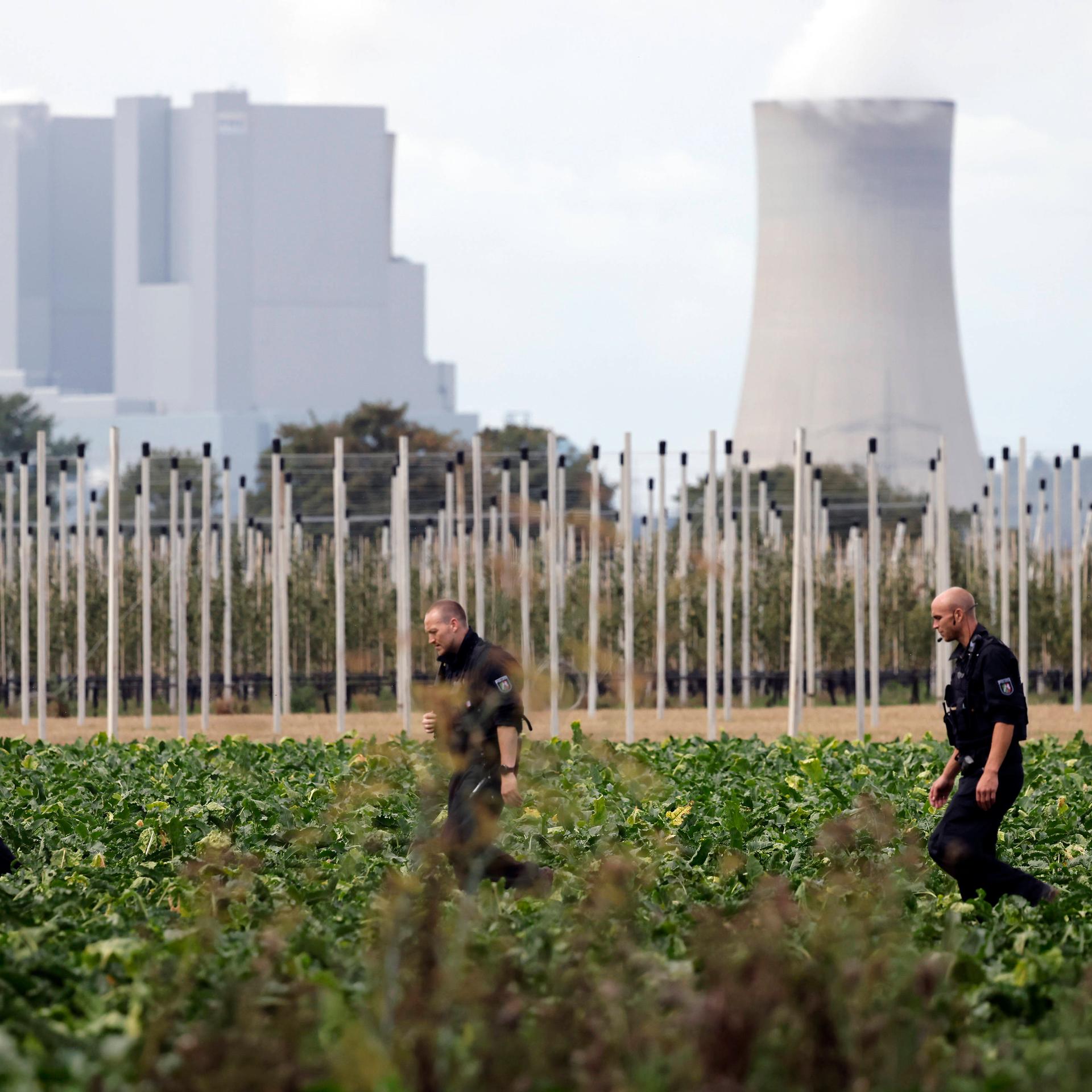 Nahe einem mutmaßlichen Anschlag auf ein Umspannwerk nahe Bergheim bei Köln durchsuchen Polizisten umliegende Felder. Im Hintergrund ist ein Kraftwerk zu sehen.