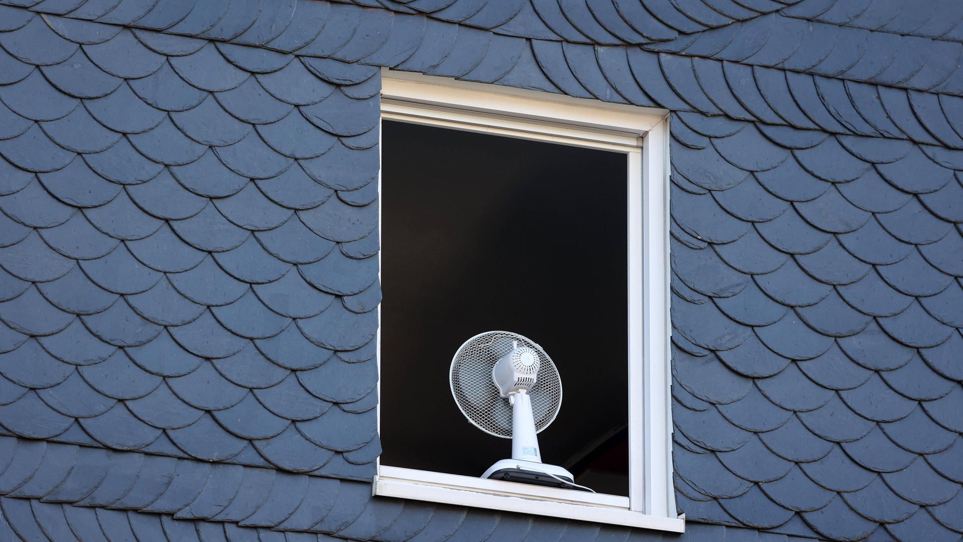 Nach einer sehr warmen Nacht ist ein Fenster in einem Haus am Morgen komplett geöffnet, um die Wohnung zu lüften. Auf dem Fensterbrett steht ein Ventilator. Nach einer sehr warmen Nacht ist ein Fenster in einem Haus am Morgen komplett geöffnet, um die Wohnung zu lüften. Auf dem Fensterbrett steht ein Ventilator.