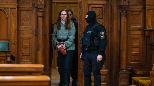 Maja T. betritt den Gerichtssaal in Budapest. Neben ihr steht ein vermummter Sicherheitsbeamter 