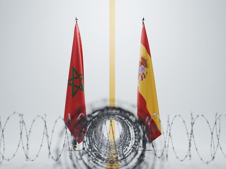 Die Flaggen von Marokko und Spanien, getrennt durch eine gelbe Linie hinter scharf gewundenem Stacheldraht vor weißem Hintergrund.