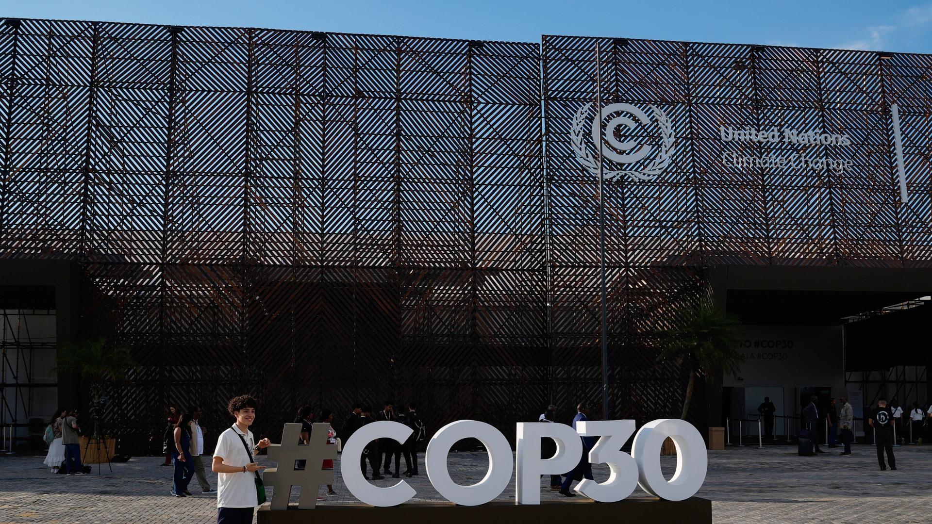 Eine Person posiert am Samstag, dem 8. November 2025, in Belém, Brasilien, für ein Foto vor einem Schild des UN-Klimagipfels COP30.