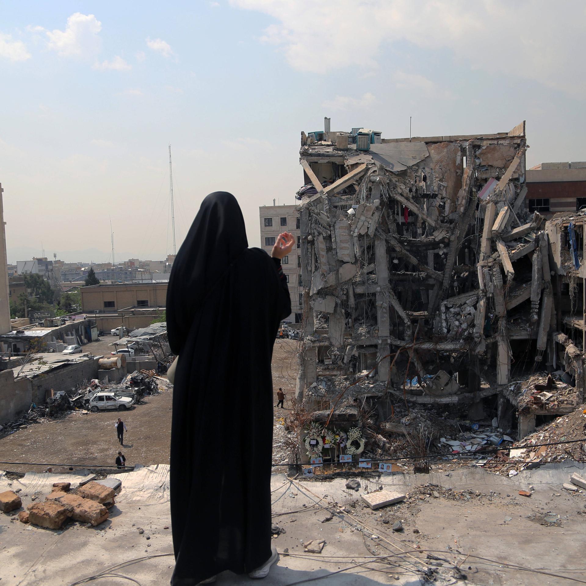 Frau blickt auf zerstörtes Haus in Iran.