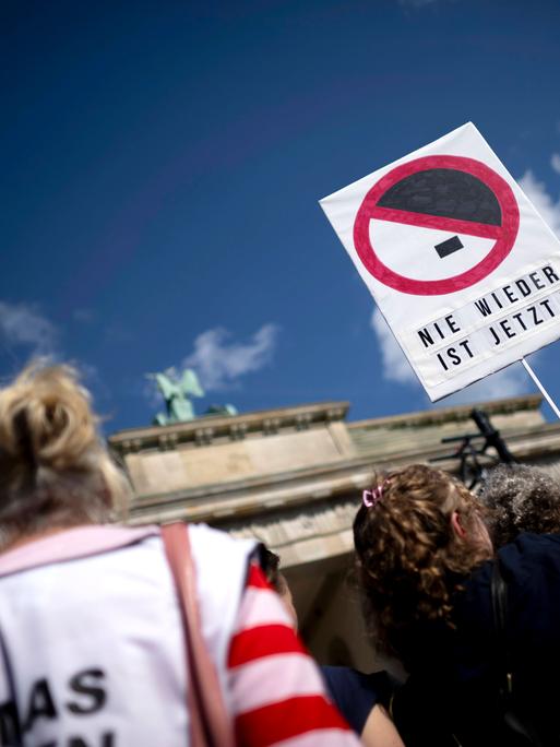 Demonstration gegen Rechtsextremismus vor dem Brandenburger Tor in Berlin; im Fokus hält eine Person ein Schild mit der Aufschrift „NIE WIEDER IST JETZT!“ unter einem durchgestrichenen Hitler-Schnitt. Demonstration gegen Rechtsextremismus vor dem Brandenburger Tor in Berlin; im Fokus hält eine Person ein Schild mit der Aufschrift „NIE WIEDER IST JETZT!“ unter einem durchgestrichenen Hitler-Schnitt.