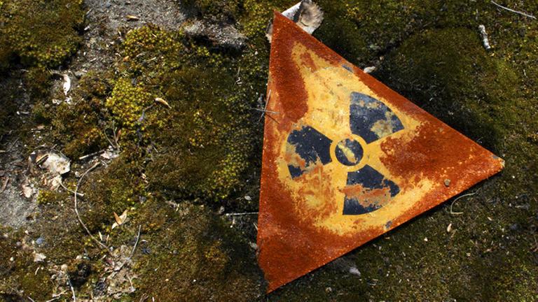 Blick auf das auf dem Boden liegende dreieckige Schild. Es zeigt das schwarze Atomsymbol auf gelbem Grund. 