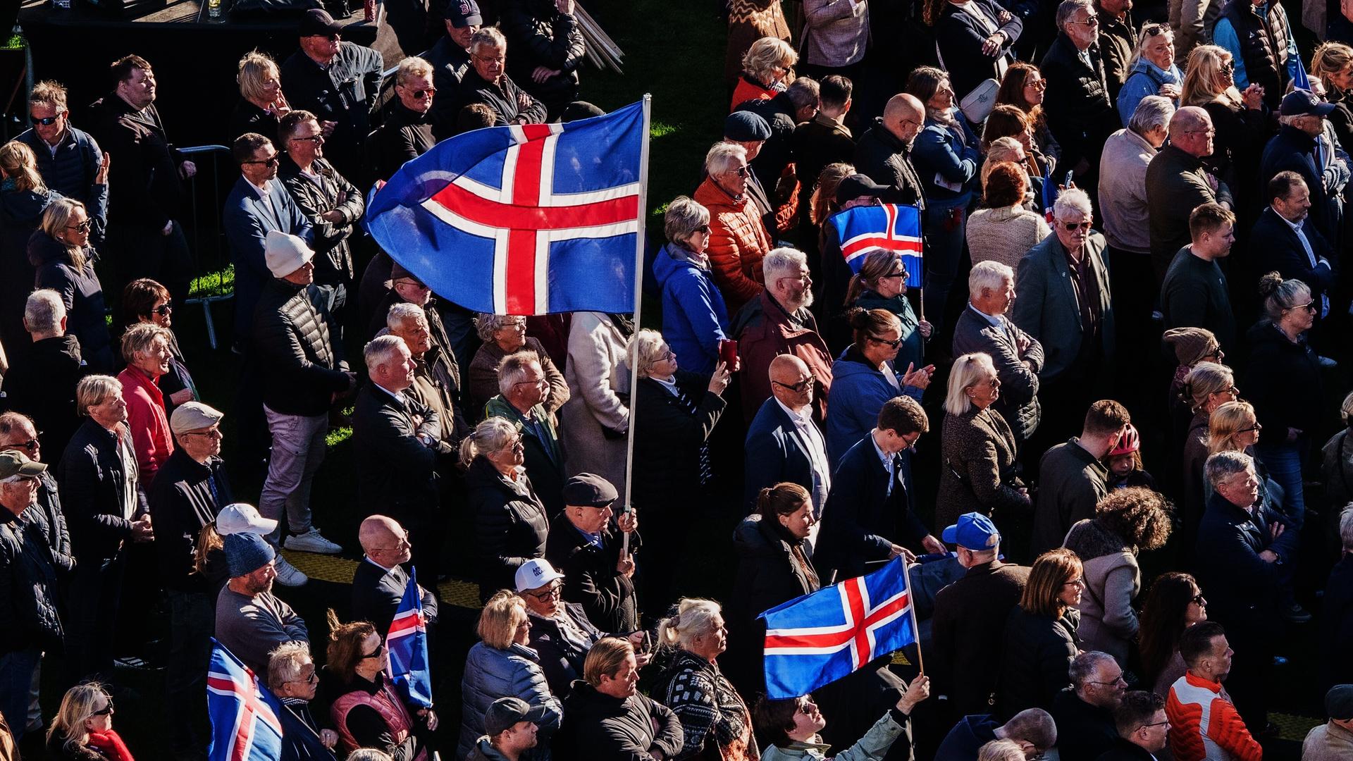 In Islands Hauptstadt Reykjavík stehen viele Menschen bei einer Kundgebung zusammen. Manche haben Island-Flaggen bei sich. In Islands Hauptstadt Reykjavík stehen viele Menschen bei einer Kundgebung zusammen. Manche haben Island-Flaggen bei sich.