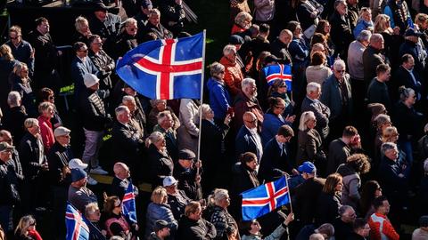In Islands Hauptstadt Reykjavík stehen viele Menschen bei einer Kundgebung zusammen. Manche haben Island-Flaggen bei sich.