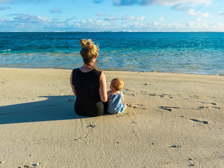 Eine Frau und ein Kind sitzen am Strand und schauen auf das Meer Eine Frau und ein Kind sitzen am Strand und schauen auf das Meer