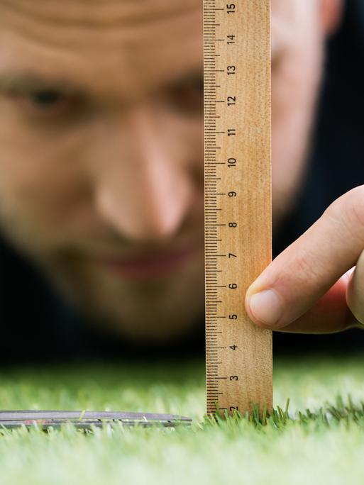 Ein Mann nutzt ein Lineal und eine Schere, um den Rasen zu schneiden.