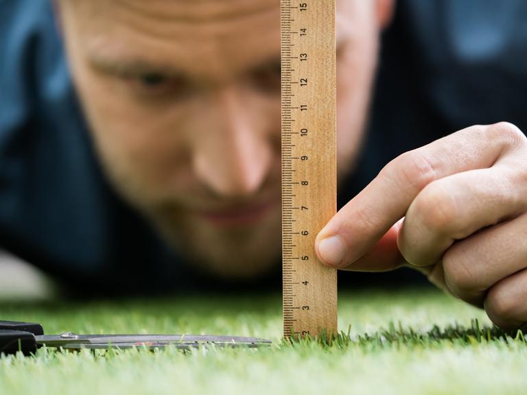 Ein Mann nutzt ein Lineal und eine Schere, um den Rasen zu schneiden.